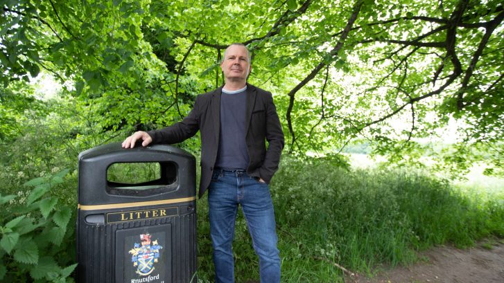 Cllr Mike Houghton stands by a bin branded as Knutsford Town Council's against a green leafy background