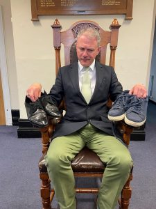mayor sat on a chair holding two pairs of shoes