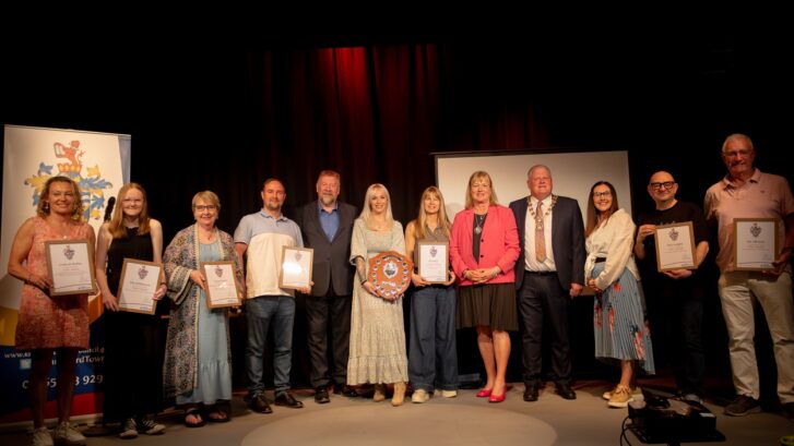 Winners of the 2025 Town Awards on stage with the Town Mayor holing their awards