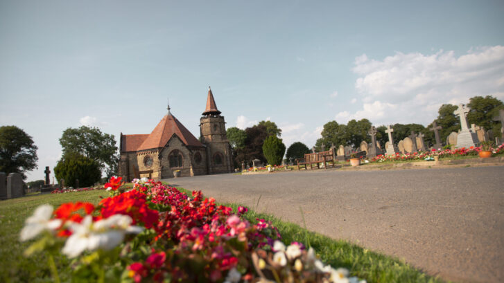 Tabley Hill Chapel. Pink and red flowers in the foreground with the chapel standing proud in the sun behind.