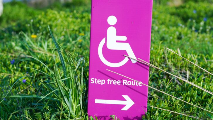 A pink accessibility logo sign with the words 'step free route' with an arrow.