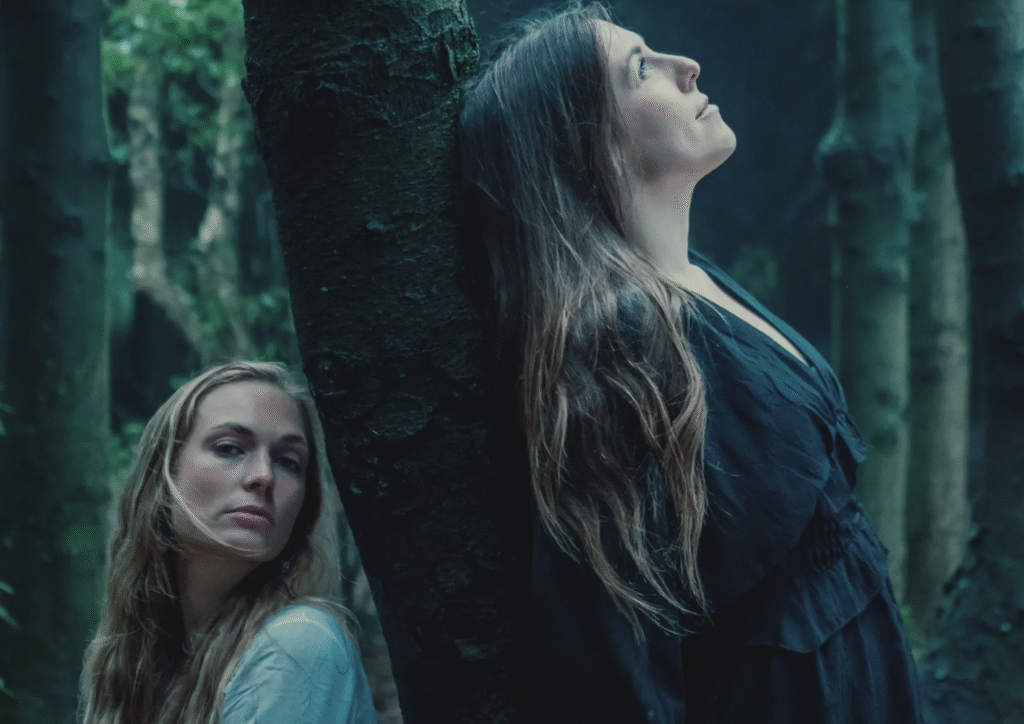 Two women leaning back to back against a tree.
