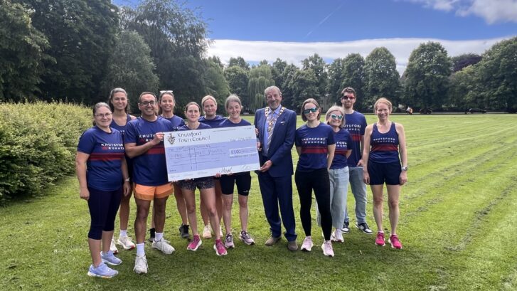 A group of people from the Knutsford Runners club stood smiling holding a large cheque for £500 with the Town Mayor of Knutsford.