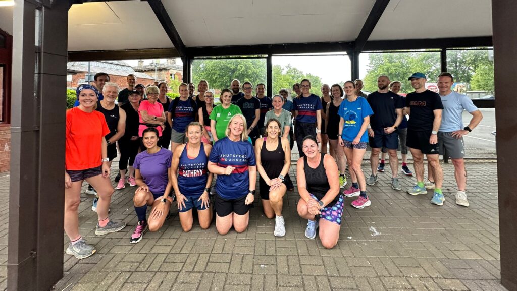 A group of people in fitness gear stood smiling under a bus shelter after finishing their group run.