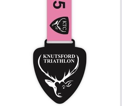 A pink and black medal featuring the text "Knutsford Triathlon" prominently displayed.