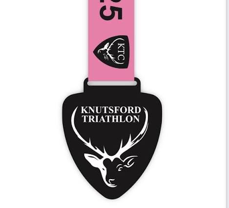 A pink and black medal featuring the text "Knutsford Triathlon" prominently displayed.
